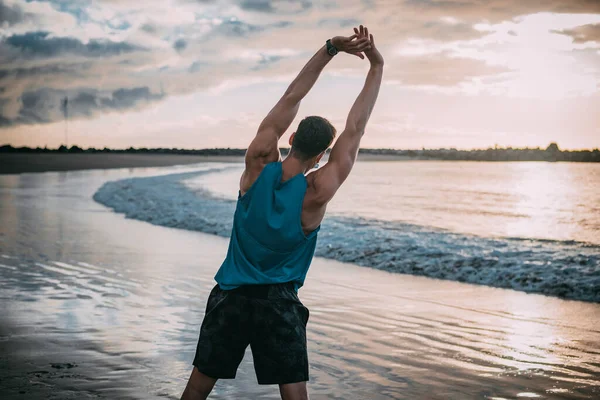 一个年轻人日落时在海滩上锻炼 温暖的色彩 图库照片
