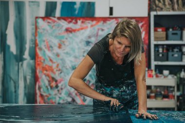 Genç bir kadın, kendi çalışma masasına elleriyle ve spatulasıyla soyut bir resim çiziyor. Kafana odaklan.