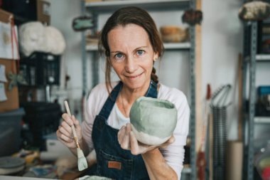 Genç zanaatkar kadın elinde bir parça seramik ile çalışıyor.