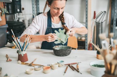 Genç zanaatkar kadın elinde bir parça seramik ile çalışıyor.