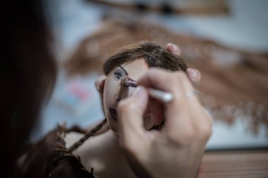 Genç bir kadın bez bebeğinin yüzünü boyuyor.