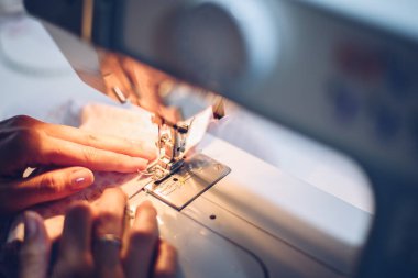 Genç, uzun saçlı bir kadın makinesiyle dikiş dikiyor.