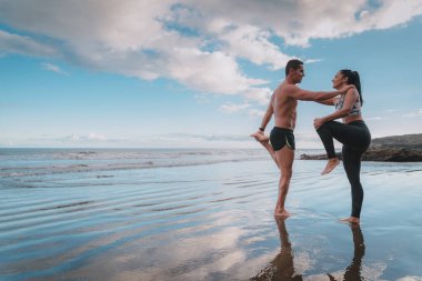 Genç adam ve kadın sahilde sağlıklı bir şekilde egzersiz yapıyorlar.