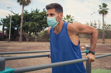 Genç adam dışarıda yüz maskesi takarak egzersiz yapıyor.