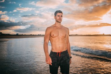 Genç bir adam plajda gün batımında egzersiz yapıyor. Sıcak renkler