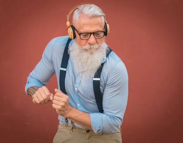an older man in hipster clothes and glasses and long white beard listens to music and dance happily in the street focus on head