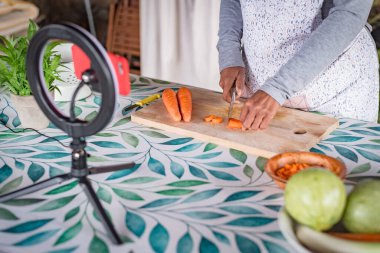 Gözlüklü siyahi kadın cep telefonu pişirme dersleriyle internetten ders veriyor.