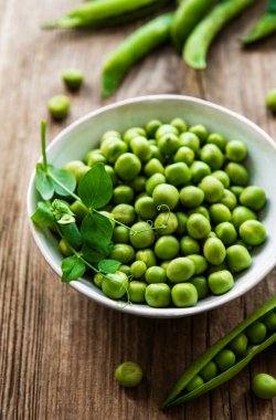 Beyaz kasede yeşil bezelyeler, ahşap masada taze kabuklar, üst ya da düz yatıyordu.