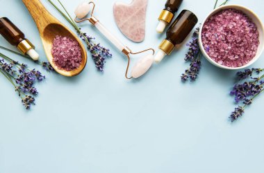 Lavantalı doğal organik SPA kozmetik. Düz banyo tuzu, spa ürünleri ve lavanta çiçekleri mavi arka planda. Cilt bakımı, güzellik tedavi konsepti