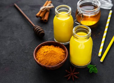 Sarı zerdeçal latte. Siyah beton zemin üzerinde tarçın, zerdeçal, zencefil ve bal içeren altın süt.