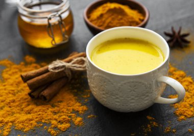 Sarı zerdeçal latte. Siyah beton zemin üzerinde tarçın, zerdeçal, zencefil ve bal içeren altın süt.