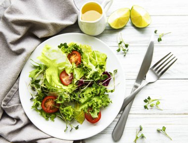 Taze yeşil salata kasesi, domatesli ve beyaz ahşap arka planda mikro yeşillikler. Sağlıklı yemek, en iyi manzara..