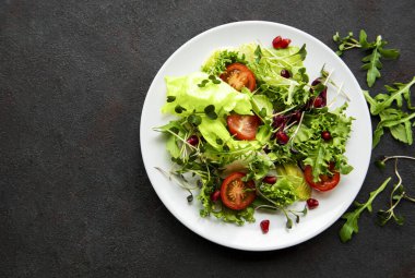 Taze yeşil salata kasesi, domatesli ve siyah beton arka planda mikro yeşillikler. Sağlıklı yemek, en iyi manzara..