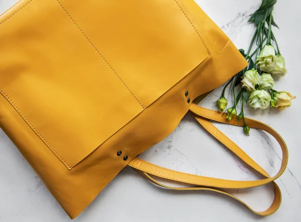 Large yellow leather bag and flowers on marble background