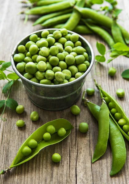 Fresh green peas in a small metal bucket on old wooden backgroun