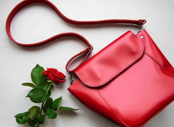 Red leather women bag and rose on gray background