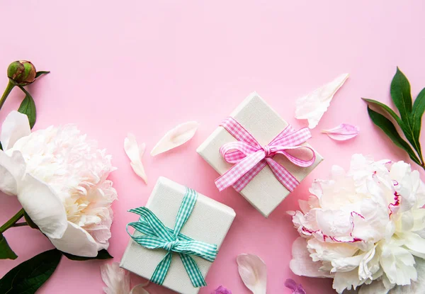 Pembe arka planda şölen kompozisyonu: şakayık çiçekleri, hediye kutuları. Üst görünüm, alanı kopyala.