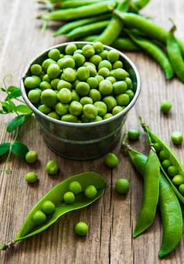 Küçük metal kovadaki taze bezelyeler eski ahşap grupta.