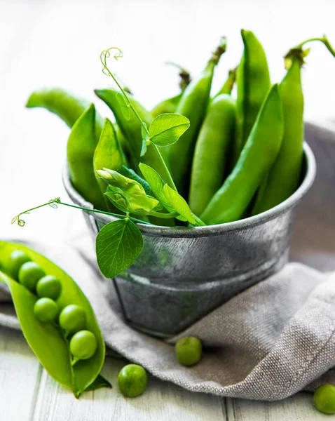 Fresh green peas in a small metal bucket on old wooden backgroun