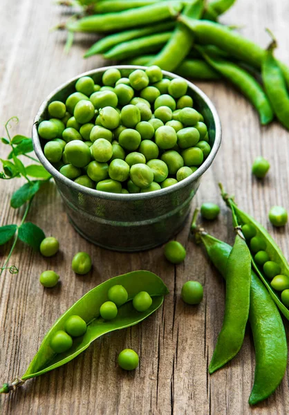 Fresh green peas in a small metal bucket on old wooden backgroun