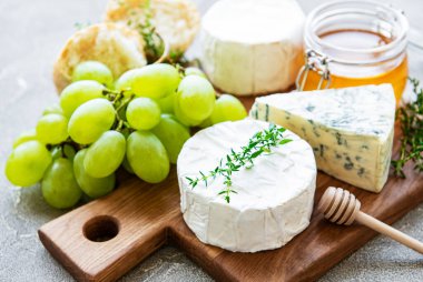 Gri beton arka planda peynir seçimi, bal ve üzüm