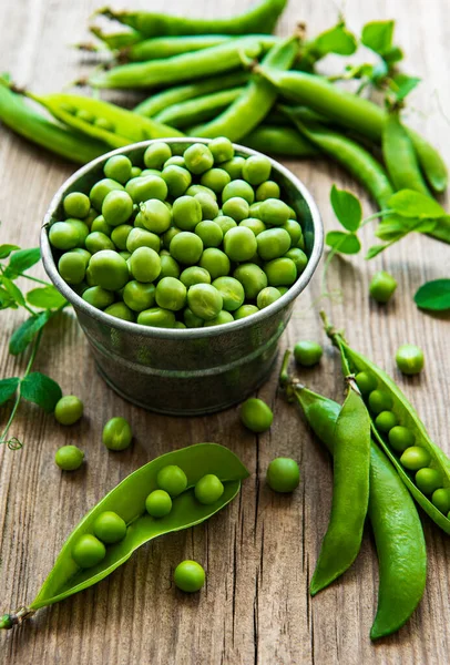 Fresh green peas in a small metal bucket on old wooden backgroun