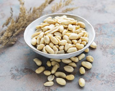 Gri beton arka planda ahşap bir kasede soyulmuş fıstıklar.