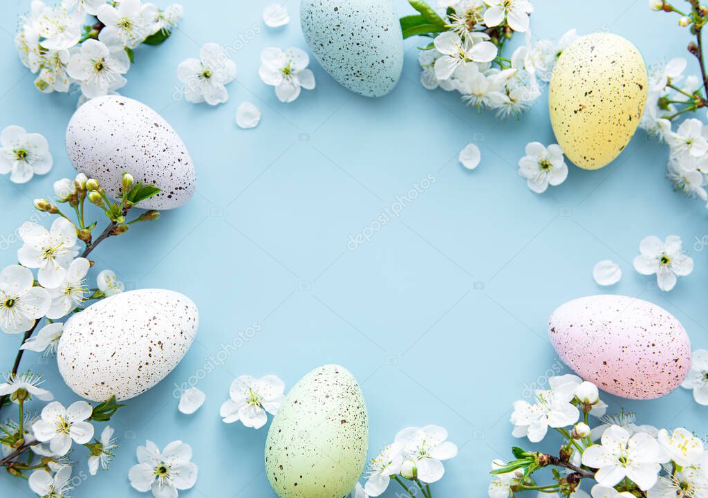 Colorful Easter eggs with spring blossom flowersover blue background. Colored Egg Holiday border. 