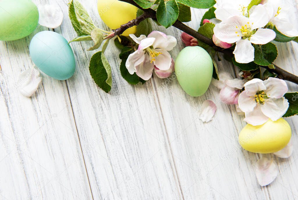 Colorful Easter eggs with spring blossom flowers over wooden background. Colored Egg Holiday border. 