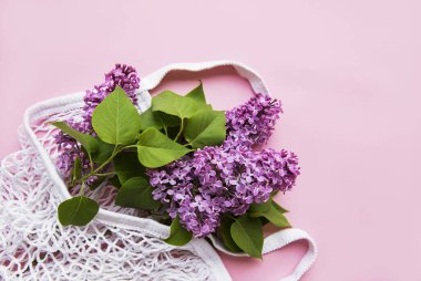 Pembe arka planda tekrar kullanılabilir eko ağ torbasında bir demet leylak. Plastik yok, sıfır atık. Tebrik kartı, kartpostal, davetiye için Üst Görünüm Şablonunu kopyala.