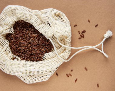 Kahverengi arka planda pamuk torba içinde çiğ kırmızı pirinç. 