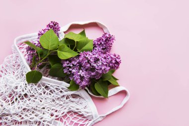 Pembe arka planda tekrar kullanılabilir eko ağ torbasında bir demet leylak. Plastik yok, sıfır atık. Tebrik kartı, kartpostal, davetiye için Üst Görünüm Şablonunu kopyala.