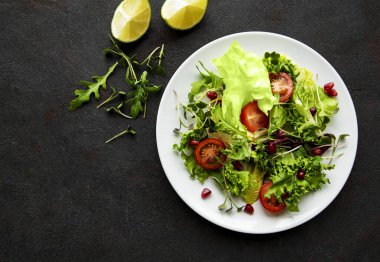Taze yeşil salata kasesi, domatesli ve siyah beton arka planda mikro yeşillikler. Sağlıklı yemek, en iyi manzara..