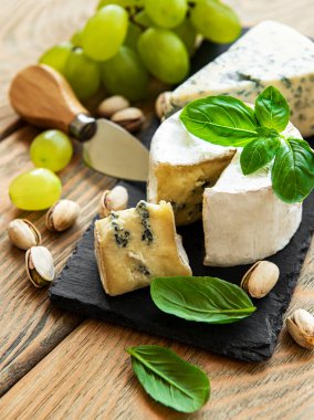 Eski ahşap bir masada çeşitli peynir, üzüm ve fındık çeşitleri.