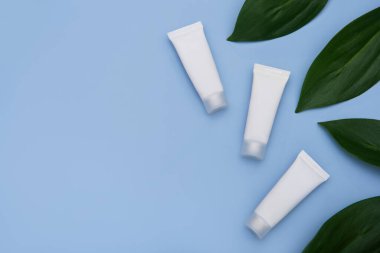 Mavi arka planda yeşil yapraklı beyaz krem tüpleri.