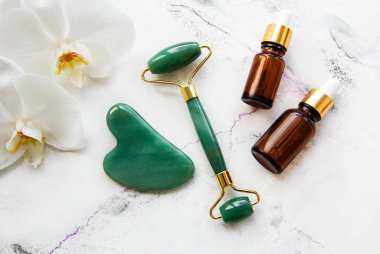 Beyaz mermer arka planda kozmetik ürünü ile yüz masajı yeşim silindiri