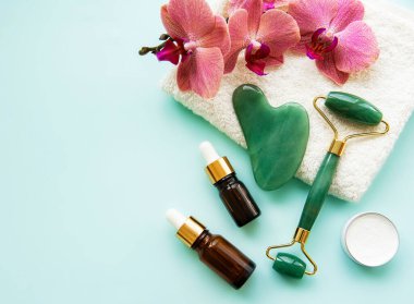 Pastel yeşil arka planda kozmetik ürünü olan yüz masajı yeşim silindiri.