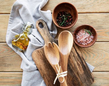 Eski mutfak gereçleri. Tahta kaşıklar, tahta kesme tahtası, eski ahşap masa üzerinde peçete ve baharatlar. Üst görünüm