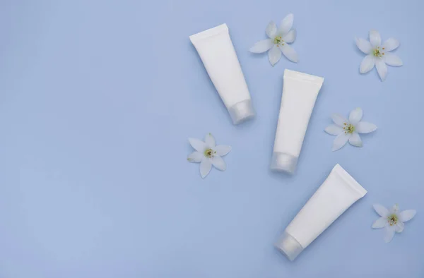 White tubes of cream on a blue background with white flowers