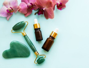 Pastel yeşil arka planda kozmetik ürünü olan yüz masajı yeşim silindiri.