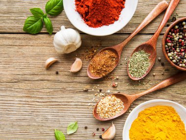 Tahta bir masada, kâselerde ve kaşıklarda çeşitli renklerde baharatlar var.