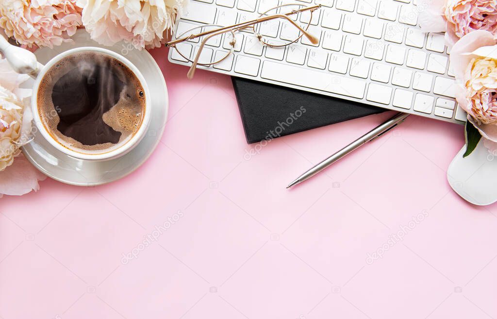 Flat lay top view women's office desk with flowers. Female workspace with laptop, flowers peonies, accessories, notebook, glasses, cup of coffee on pink background. Holiday background.Copy space