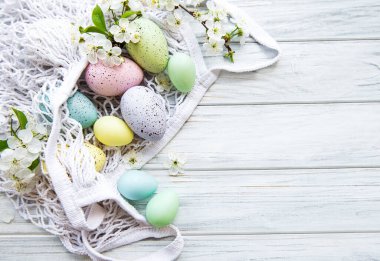 Paskalya yumurtaları ve bahar çiçekleriyle dolu bir ip torbası kırsal bir tahta masanın köşesinde.