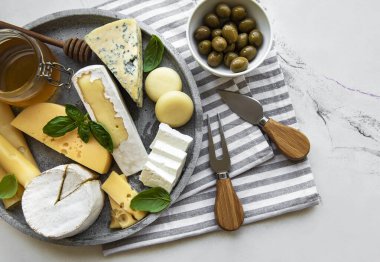 Mermer arka planda çeşitli peynir, üzüm, bal ve atıştırmalıklar var.