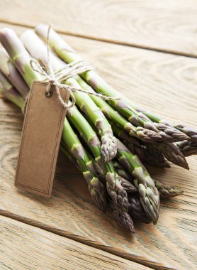 Eski ahşap masada boş etiketli taze yeşil kuşkonmaz. Düz yatıyordu