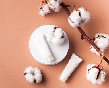 Kahverengi arka planda beyaz krem tüpleri ve pamuk çiçekleriyle dekoratif dallar.