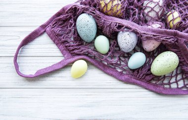 Paskalya yumurtaları ve bahar çiçekleriyle dolu bir ip torbası kırsal bir tahta masanın köşesinde.