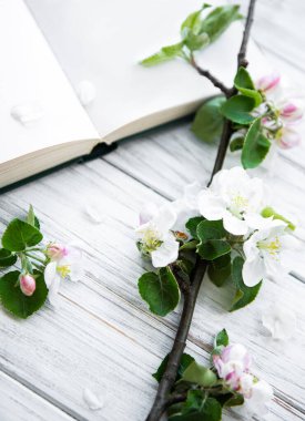 Elma ağacının çiçek açan dalının beyaz ahşap masada olduğu açık bir kitap..