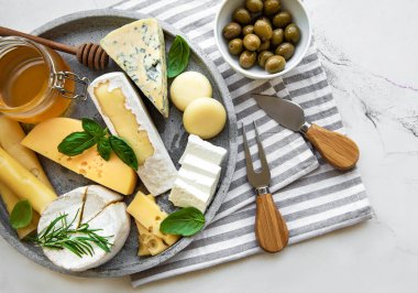 Mermer arka planda çeşitli peynir, üzüm, bal ve atıştırmalıklar var.