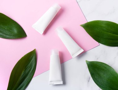 Mermer üzerine beyaz krem tüpleri ve yeşil yapraklı pembe arka plan.